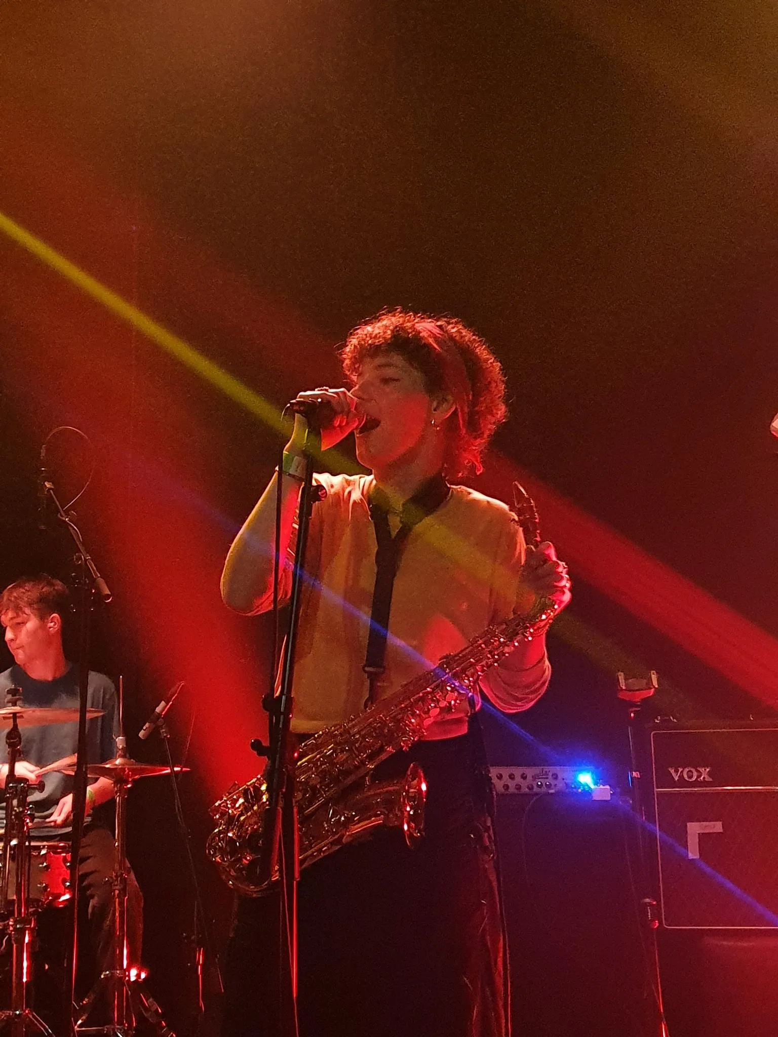 Emilia singt mit dem Saxophon in der Hand, rotes Bühnenlicht, hinten David am Schlagzeug